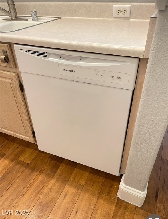 Kitchen view of white dishwasher, a sink, dark woo