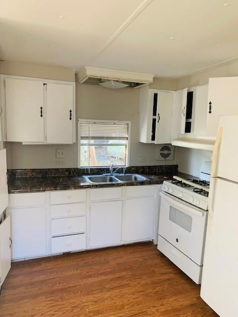 Kitchen featuring white appliances, white cabinets, dark countertops, under cabinet range hood, and wood finished floors