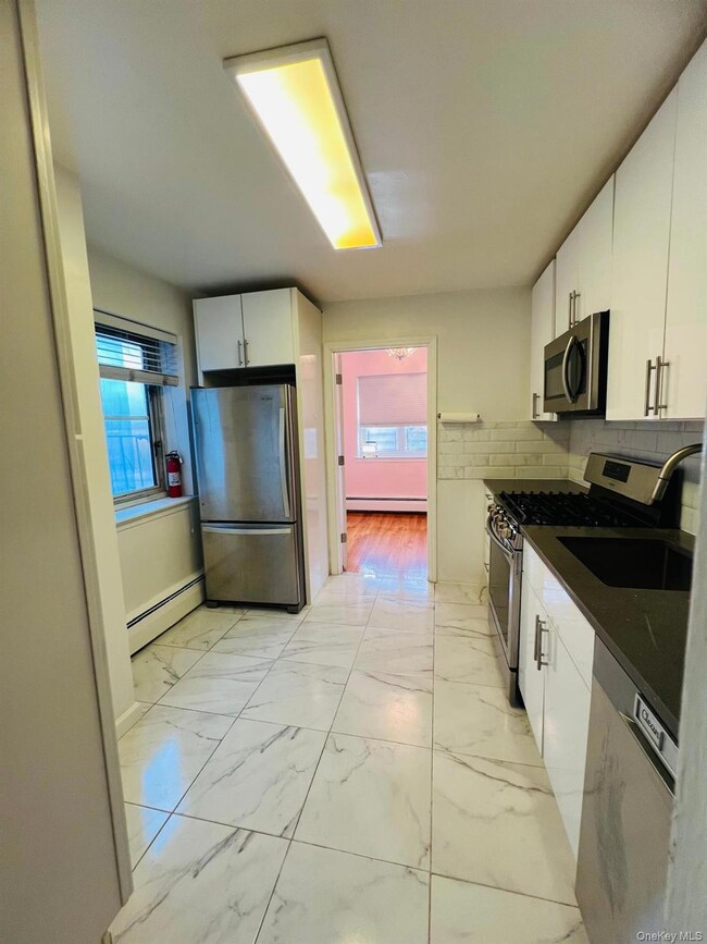 Kitchen with white cabinetry, appliances with stainless steel finishes, light marble finish floors, a baseboard heating unit, and tasteful backsplash