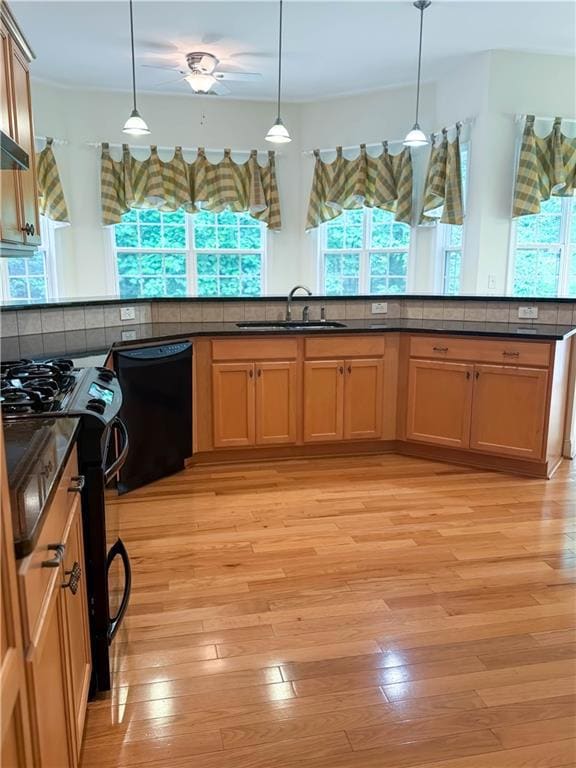 Kitchen with black appliances, a sink, dark countertops, and hanging light fixtures