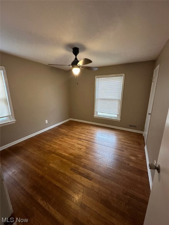 Spare room with a wealth of natural light, ceiling fan, and dark wood-type flooring