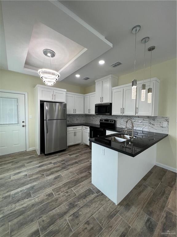 Kitchen featuring kitchen peninsula, stove, a tray ceiling, fridge, and white cabinets
