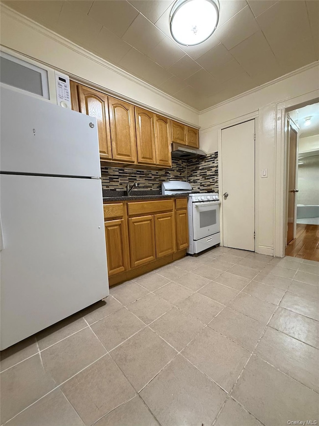 Kitchen with white appliances, crown molding, brown cabinetry, tasteful backsplash, and light tile patterned floors