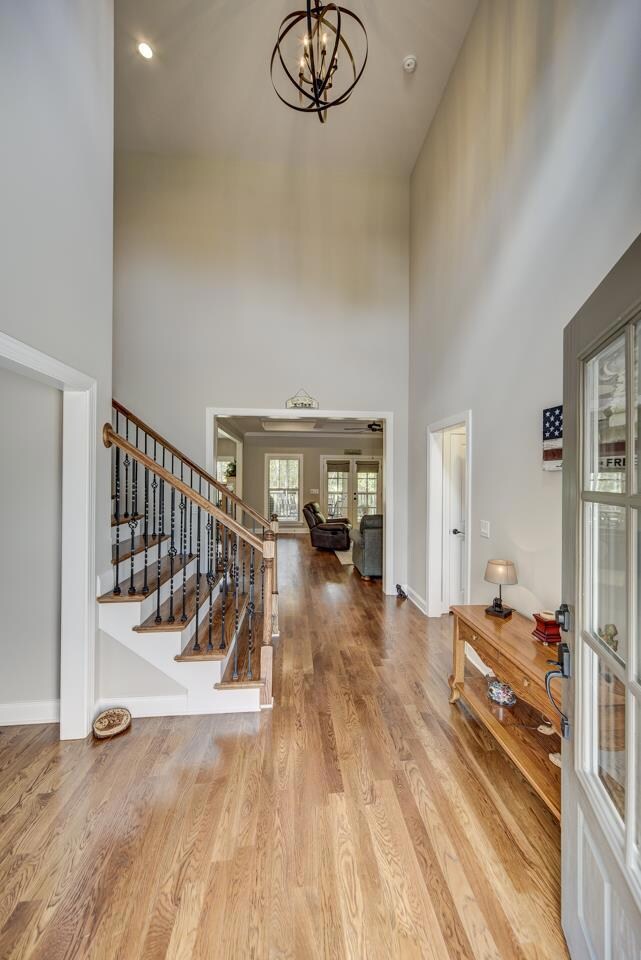 Open front door to soaring ceilings, hardwood flooring, iron chandelier, leading to living room and view of backyard. 