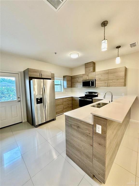 Kitchen featuring a peninsula, appliances with stainless steel finishes, light tile patterned flooring, decorative light fixtures, and modern cabinets