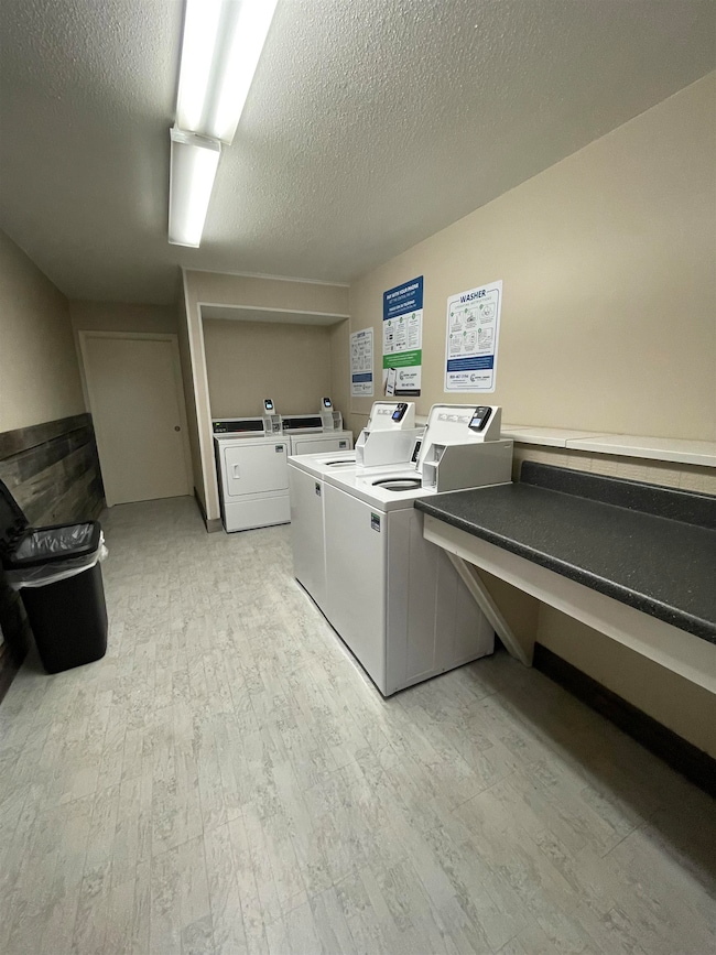 Washroom featuring light wood-type flooring, washing machine and dryer, and a textured ceiling