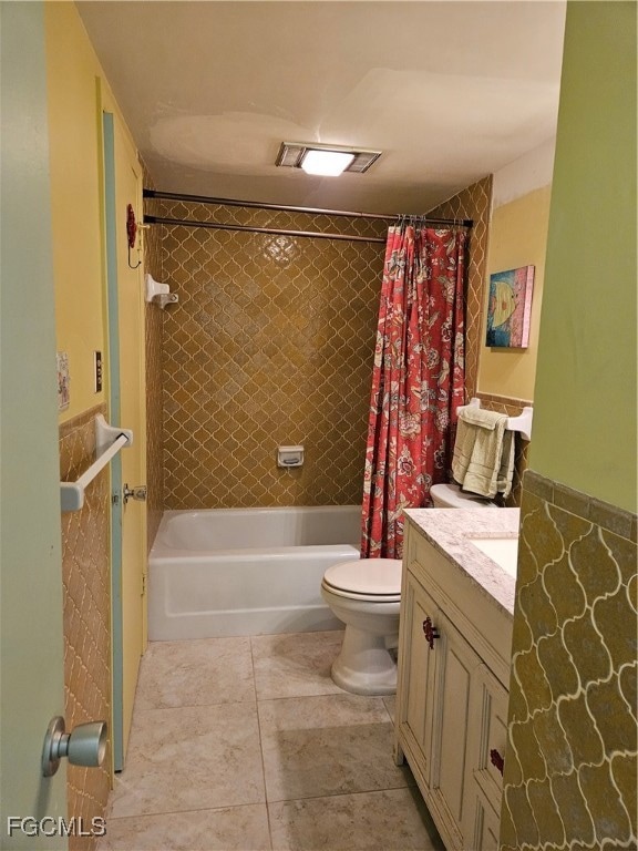 Full bath featuring shower / bath combo with shower curtain, vanity, tile walls, light tile patterned floors, and wainscoting