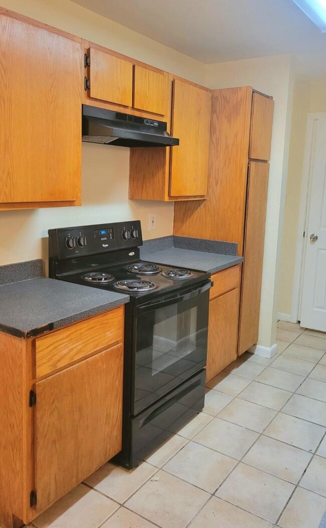 Kitchen featuring under cabinet range hood, dark countertops, light tile patterned floors, and black range with electric cooktop