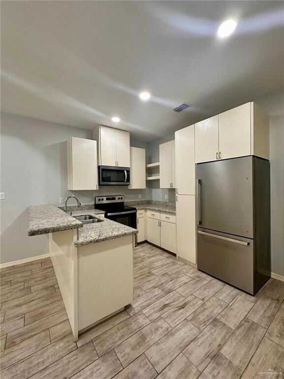 Kitchen featuring appliances with stainless steel finishes, a peninsula, recessed lighting, wood tiled floors, and light stone counters