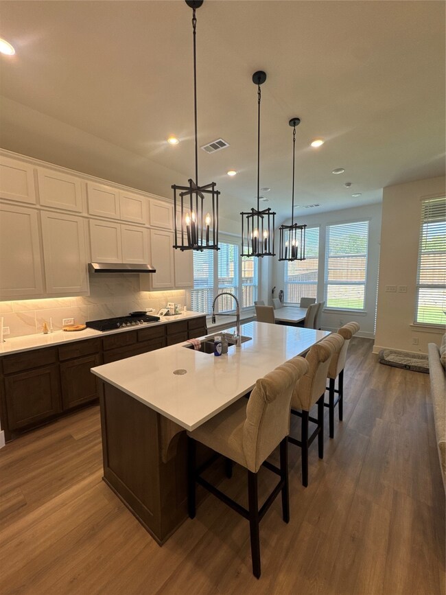 Kitchen featuring white cabinets, a breakfast bar, tasteful backsplash, dark wood finished floors, and an island with sink
