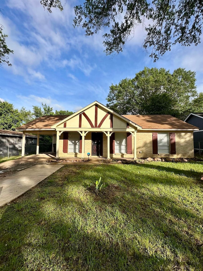 View of front of property featuring a front yard, a carport, driveway, and brick siding