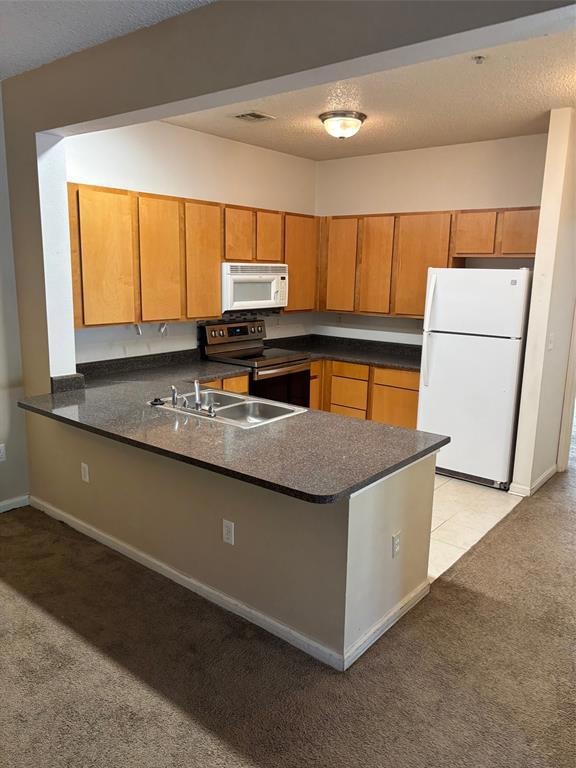 Kitchen featuring fridge, stainless steel electric range oven, light carpet, dark countertops, and brown cabinetry