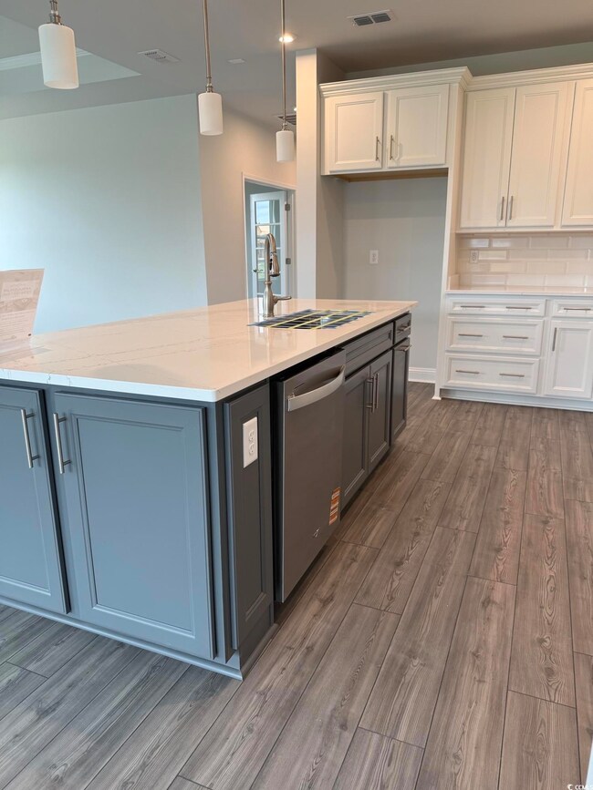 Kitchen with white cabinetry, wood finished floors, dishwasher, and hanging light fixtures