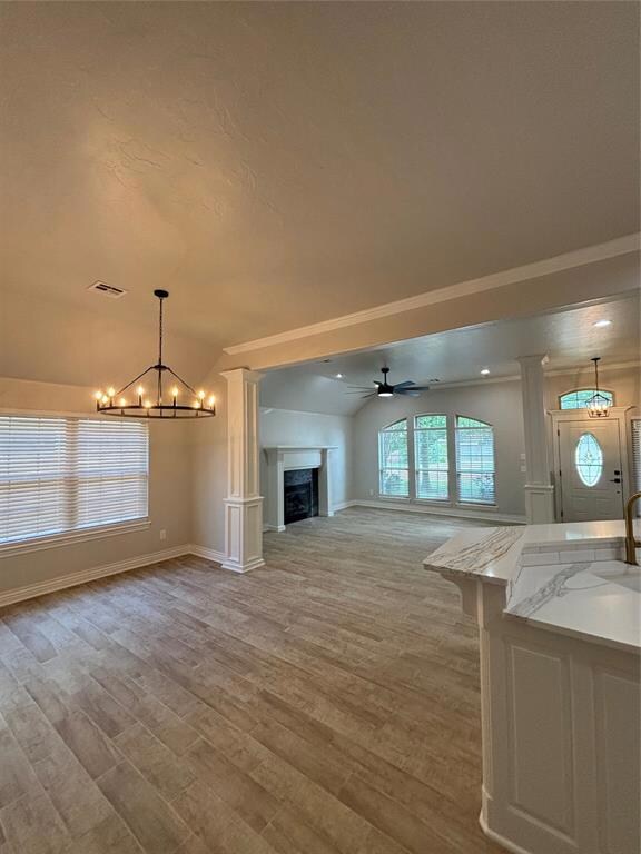 Unfurnished living room featuring a chandelier, baseboards, a ceiling fan, light wood-style flooring, and a fireplace