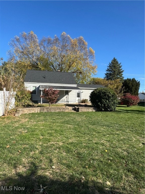 Back of house featuring a lawn and roof with shingles
