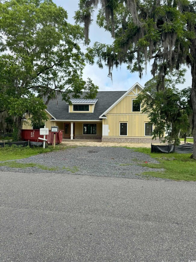 View of front of property with a shingled roof, gravel driveway, and board and batten siding