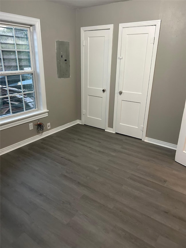 Unfurnished bedroom with electric panel and dark wood-style floors