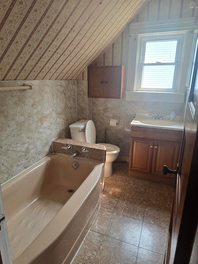 Bathroom with lofted ceiling, vanity, a bath, wallpapered walls, and tile walls