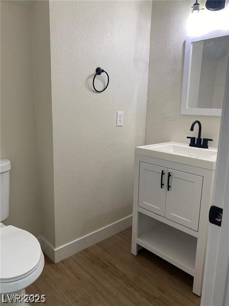 Half bath with a textured wall, dark wood-style floors, and vanity