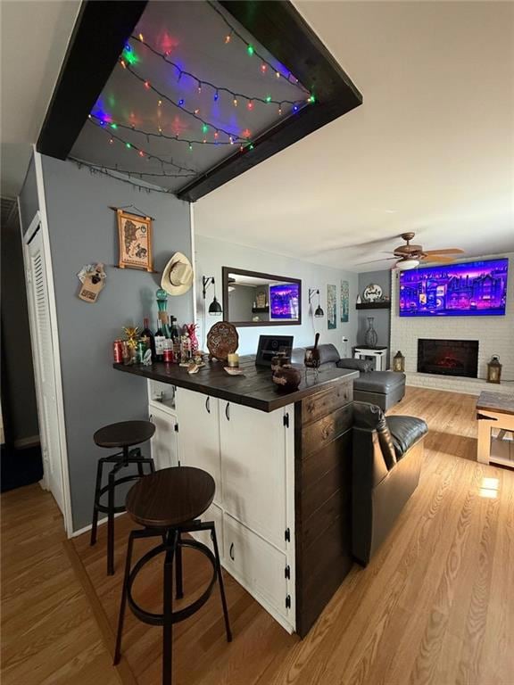 Indoor bar featuring a fireplace, light wood-style flooring, dark countertops, and ceiling fan