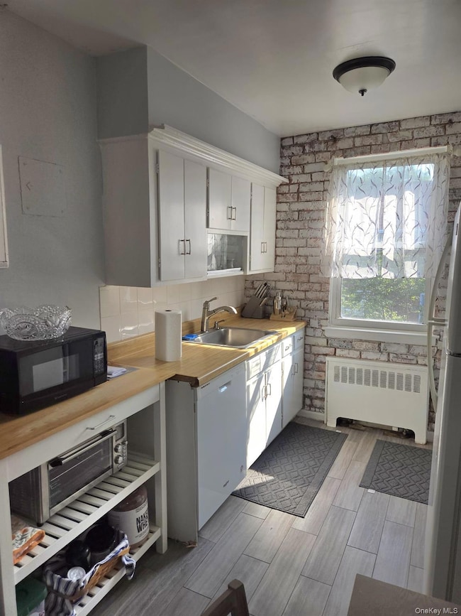 Kitchen featuring white cabinets, radiator heating unit, white appliances, wood finish floors, and backsplash