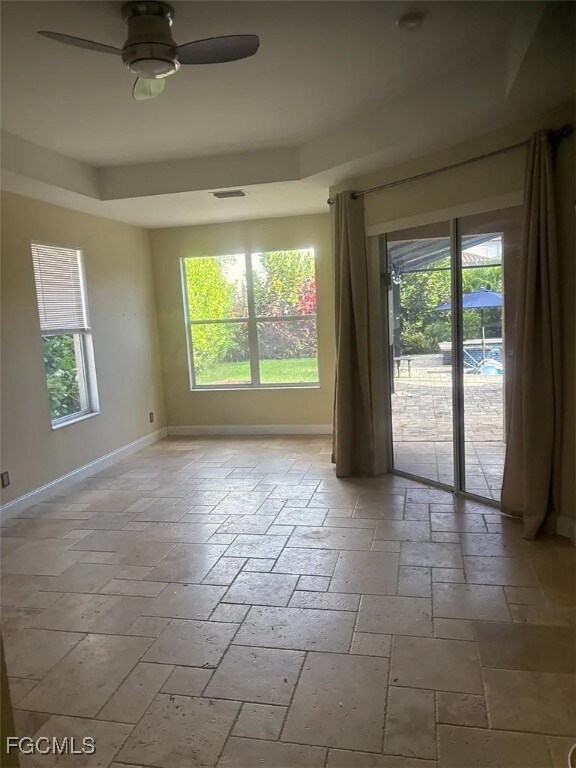 Empty room featuring stone tile floors, a raised ceiling, and ceiling fan