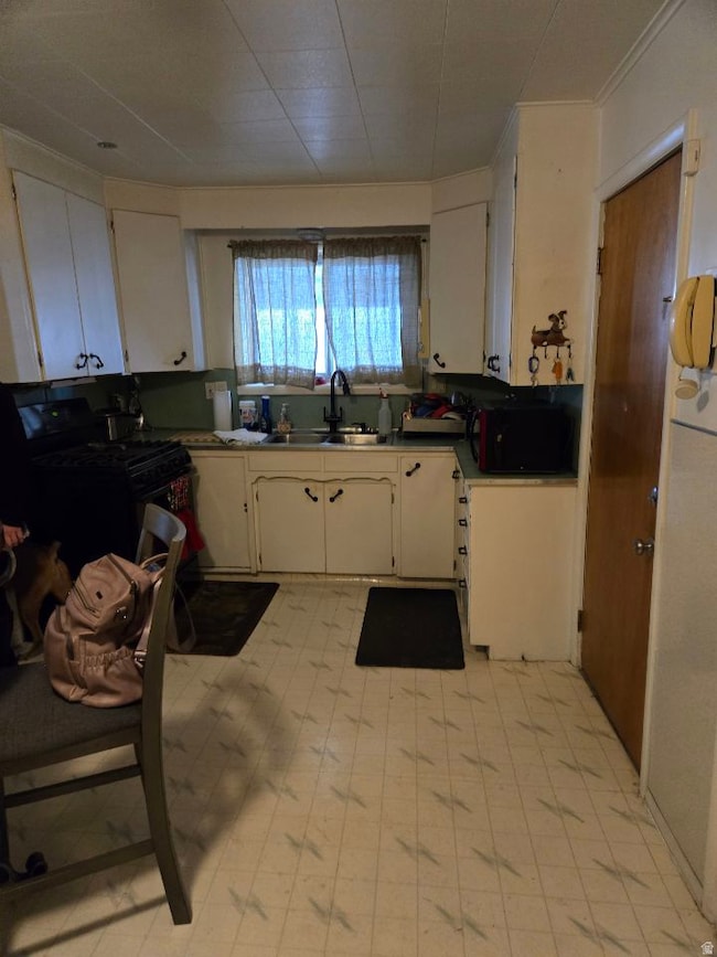 Kitchen featuring light floors, black appliances, white cabinets, and crown molding