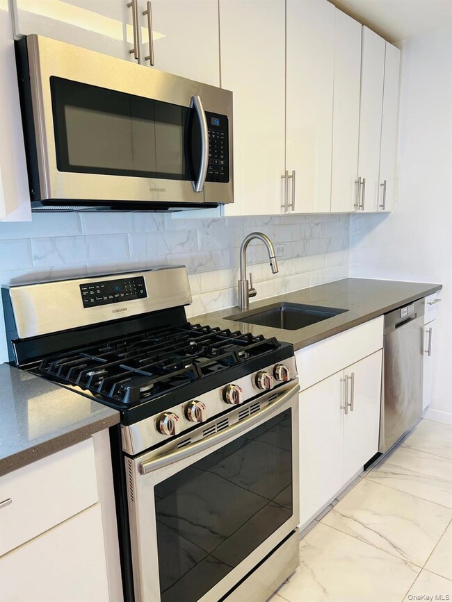 Kitchen with stainless steel appliances, decorative backsplash, dark stone countertops, and white cabinetry