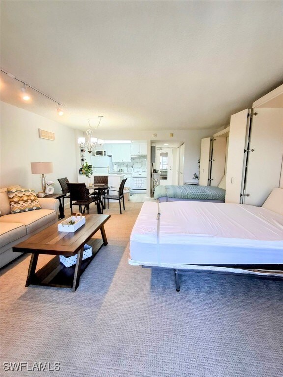 Bedroom with track lighting, a chandelier, light colored carpet, and freestanding refrigerator