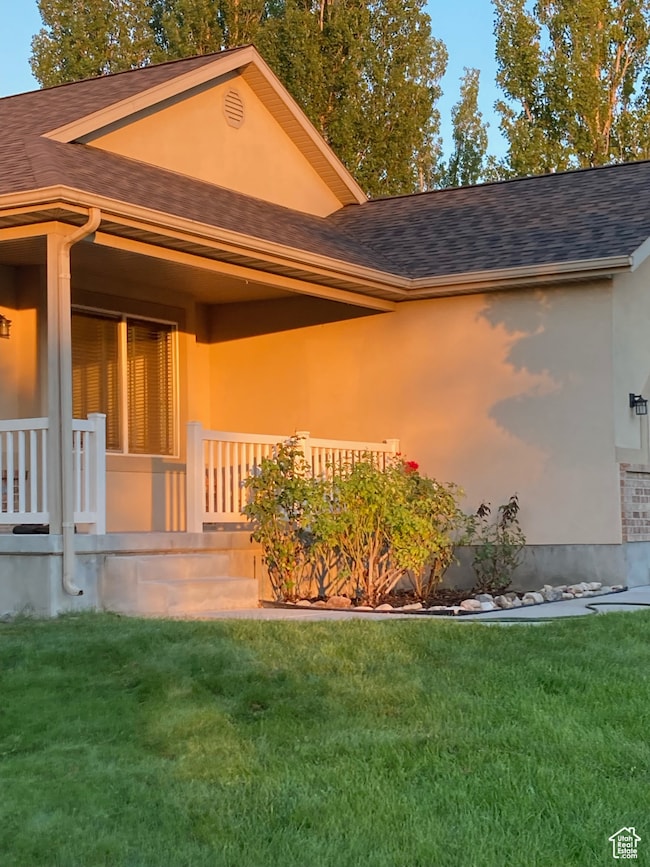 View of exterior entry with roof with shingles, a porch, and a lawn