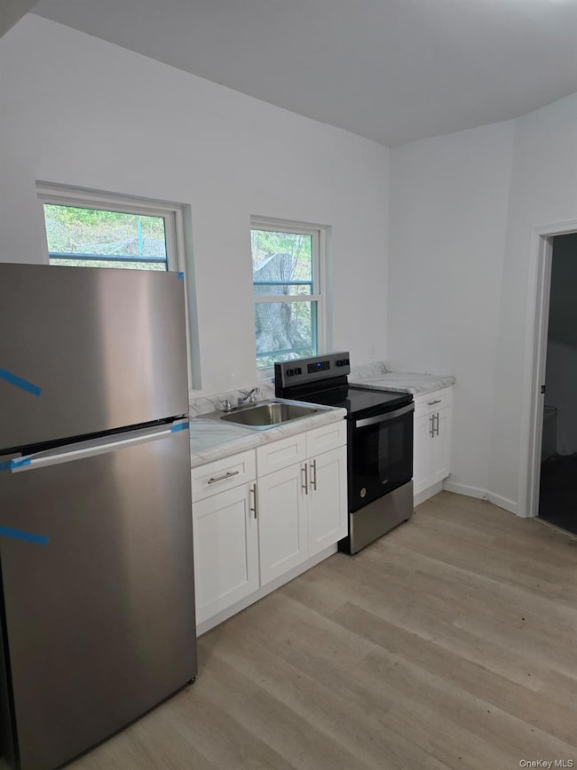 Kitchen featuring white cabinetry, appliances with stainless steel finishes, light wood-style flooring, and light stone countertops