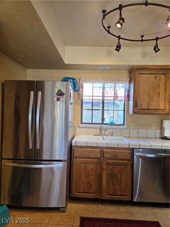Kitchen featuring tile countertops, a sink, stainl