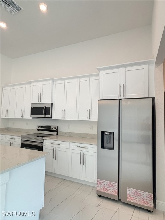 Kitchen featuring appliances with stainless steel finishes, white cabinets, light stone counters, light marble finish floors, and recessed lighting
