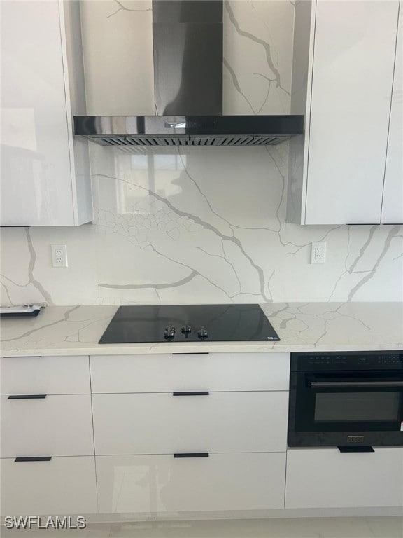 Kitchen featuring wall chimney range hood, modern cabinets, white cabinets, and light stone countertops