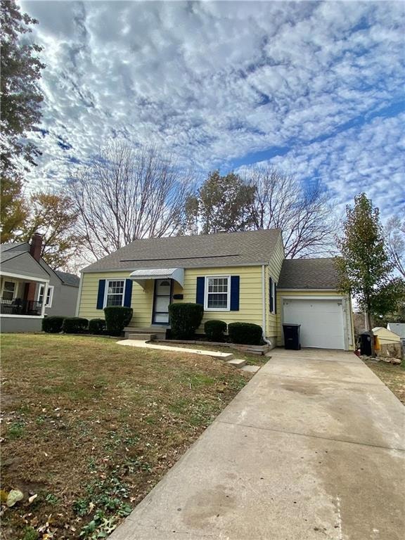 Ranch-style home with driveway, roof with shingles, an attached garage, and a front yard