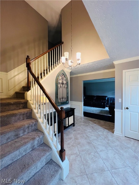 Stairs with an inviting chandelier, tile patterned flooring, and ornamental molding
