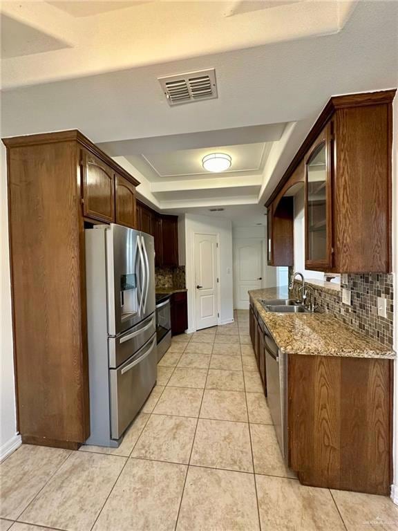Kitchen featuring stainless steel appliances, a raised ceiling, a sink, decorative backsplash, and stone counters