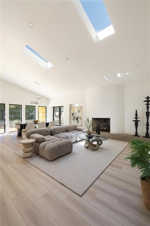 Living room featuring a skylight, a fireplace, wood finished floors, vaulted ceiling, and recessed lighting