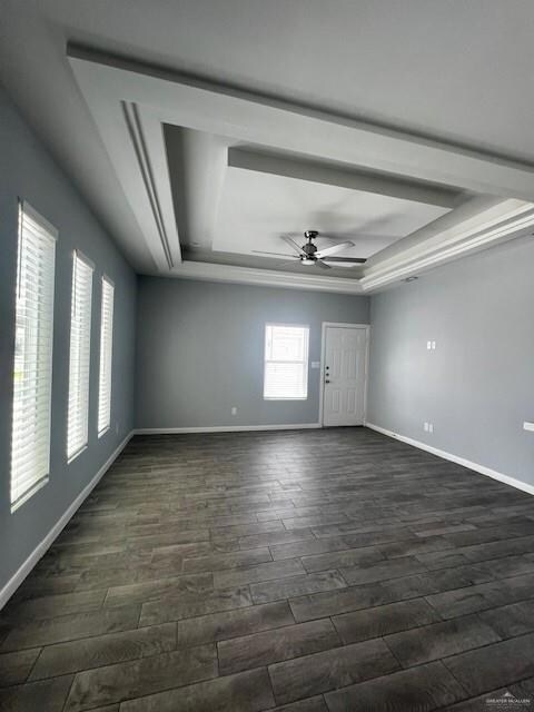 Empty room featuring dark hardwood / wood-style flooring, ceiling fan, and a tray ceiling