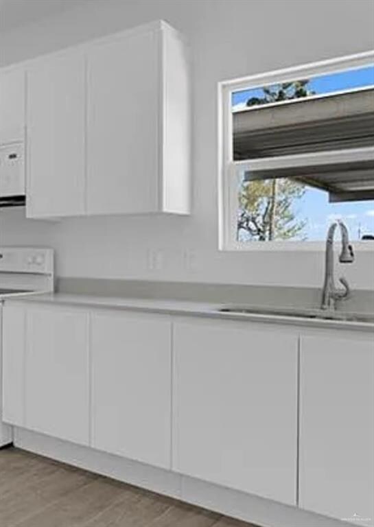Kitchen view of white cabinetry, light countertops, light wood finished floors, and white appliances