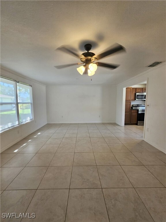 Unfurnished living room featuring ceiling fan, a textured ceiling, light tile patterned floors, and ornamental molding
