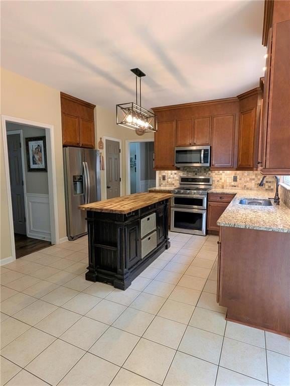 Kitchen with appliances with stainless steel finishes, butcher block countertops, tasteful backsplash, light tile patterned floors, and hanging light fixtures