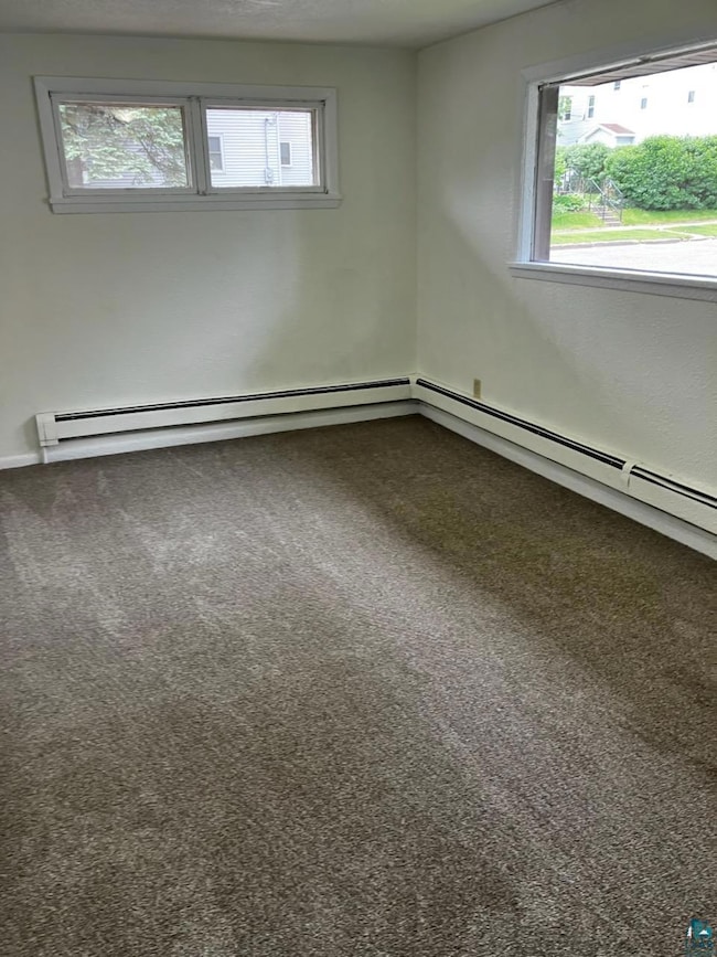 Unfurnished room featuring plenty of natural light, dark colored carpet, and baseboard heating
