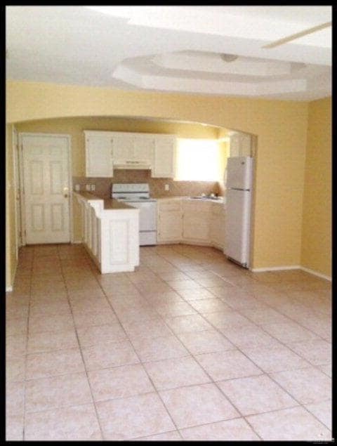 Kitchen with white appliances, light tile patterned floors, light countertops, a peninsula, and arched walkways