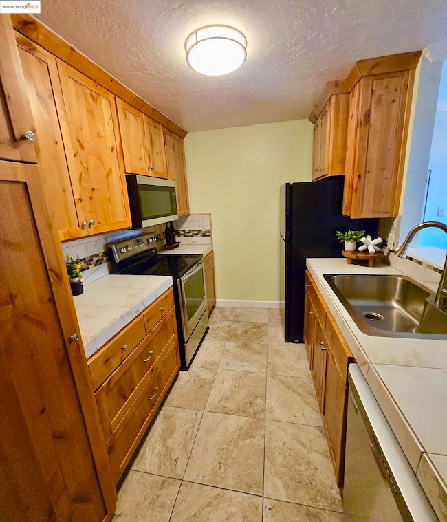 Kitchen featuring a textured ceiling, stainless steel appliances, decorative backsplash, light tile patterned floors, and tile counters