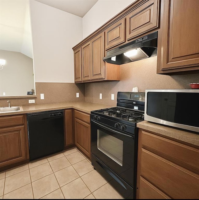 Kitchen featuring black appliances, under cabinet range hood, light tile patterned floors, decorative backsplash, and light countertops
