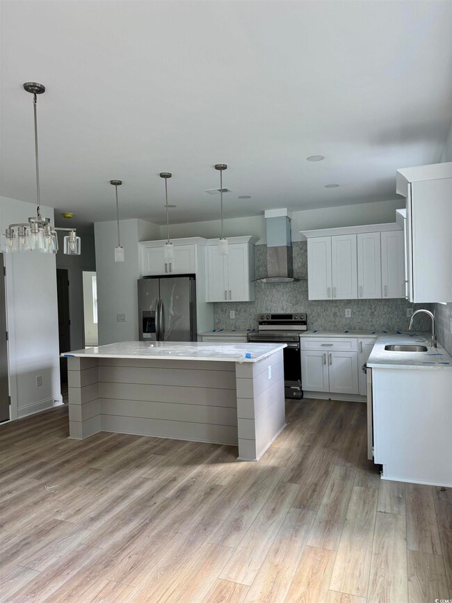 Kitchen with wall chimney exhaust hood, stainless steel appliances, a center island, and light countertops