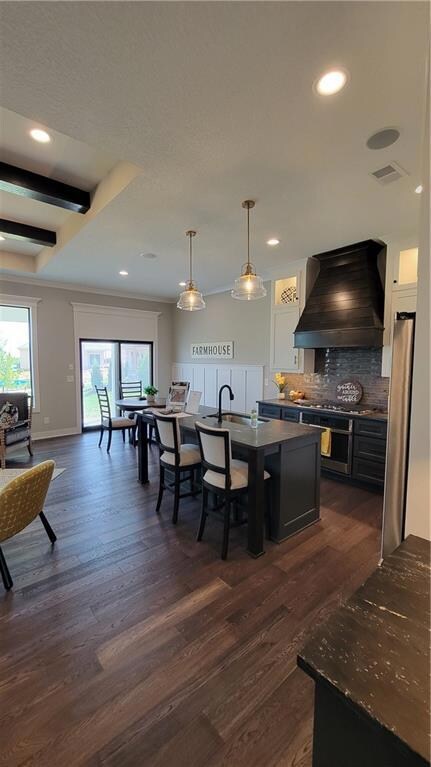 Kitchen featuring decorative light fixtures, dark wood-type flooring, exhaust hood, and backsplash