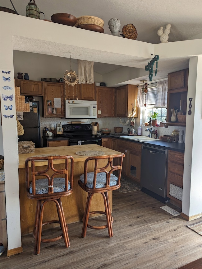 Kitchen with hardwood / wood-style floors, sink, decorative backsplash, and black appliances