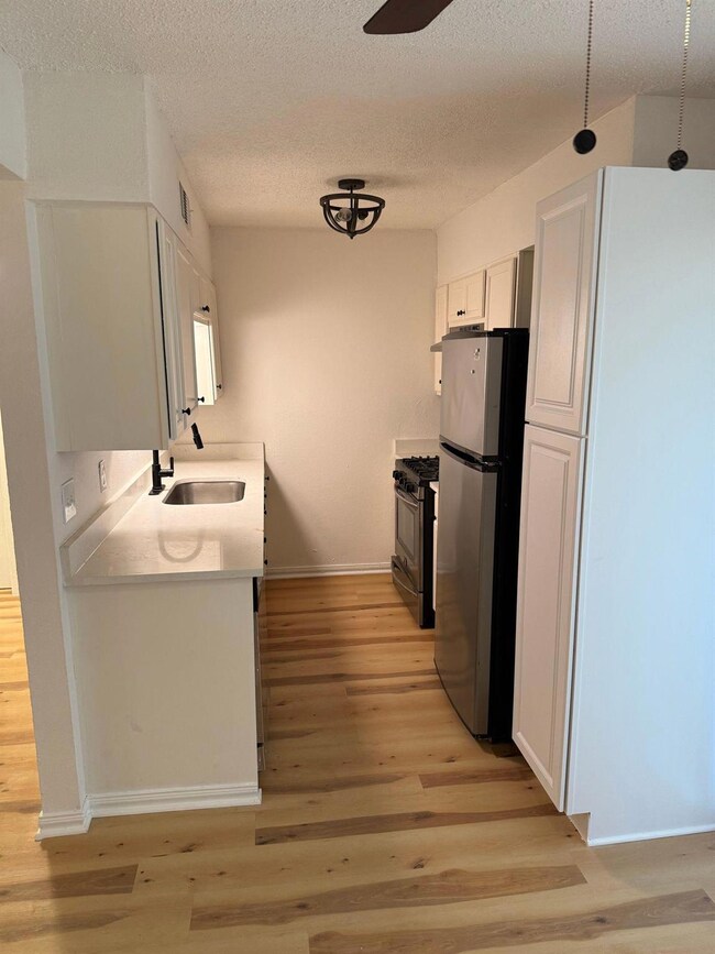 Kitchen with white cabinetry, a textured ceiling, stainless steel appliances, light wood-style flooring, and light stone counters